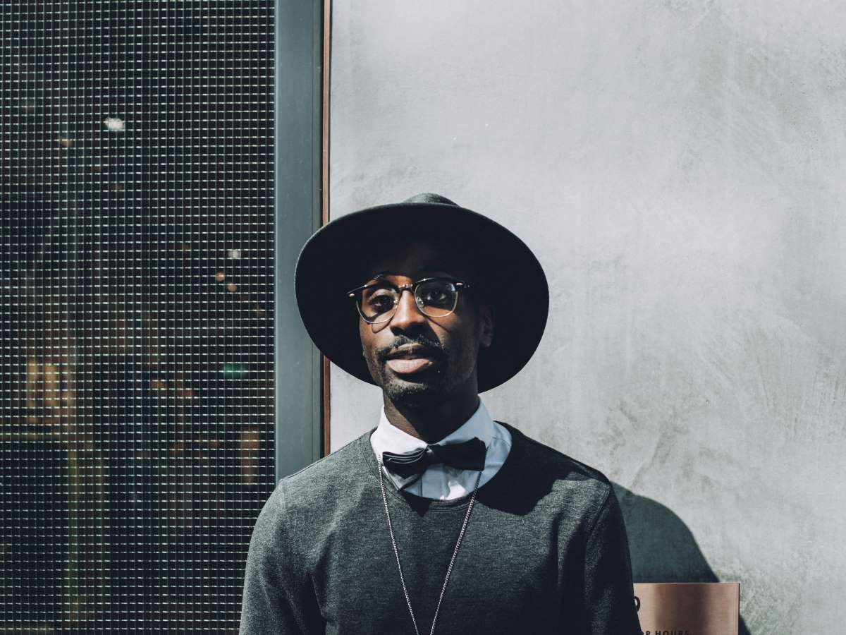 an african american man with a bowtie and hat looking at the camera